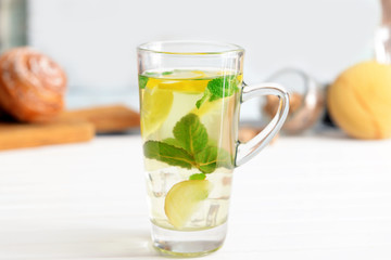 Glass cup of cold mint tea with lemon and ginger on table