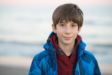 Young boy posing at the winter beach. Cute smiling happy 11 years old boy at seaside, looking at...
