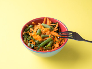 Healthy salad of grated carrots green bean arugula on yellow background