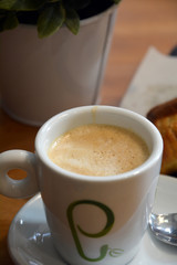 Cup of foamy cappuccino on a plate on a wooden table.