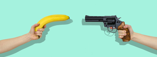 Naklejka premium hand with a banana and a hand with gun isolated on mint