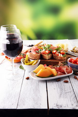 Italian antipasti wine snacks set. Cheese variety, Mediterranean olives, pickles, Prosciutto di Parma, tomatoes, artichokes and wine in glasses