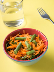Healthy salad of grated carrots green bean arugula on yellow background