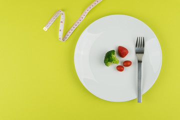 Diet concept : small amount of food on the white plate with a measuring tape.