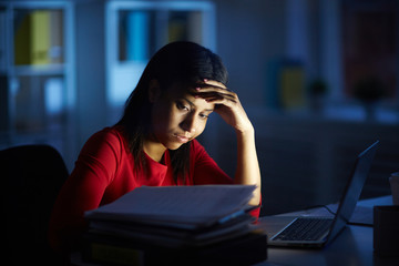 Tired businesswoman working on a laptop at her office desk late in the evening