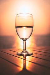Silhouette glass of wine on a wooden table with  seascape and skyline in the evening with sunset tone style.