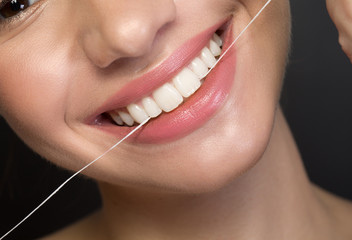 Close up of white healthy teeth of joyful young woman. She is using dental floss. Oral hygiene concept