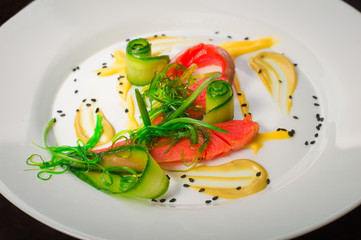 Dish with salmon, seaweed and cucumber. Old black rustic background. Top view