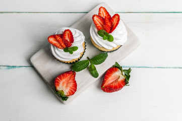 Vanilla cupcakes with butter cream and fresh strawberry on a light wooden background. Top view
