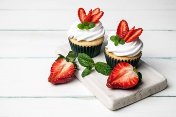 Vanilla cupcakes with butter cream and fresh strawberry on a light wooden background
