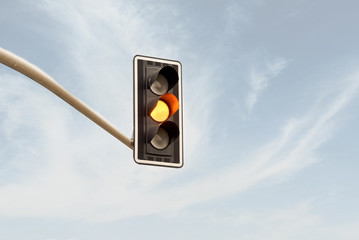 Yellow traffic light on a horizontal white metal beam, isolated on sky background
