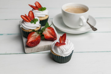 Vanilla cupcakes with butter cream and fresh strawberry and a cup of coffee on a light wooden...