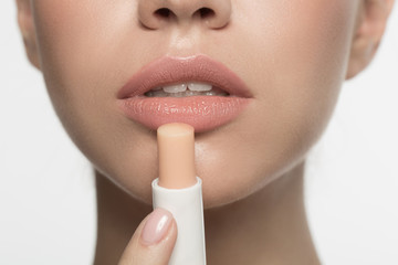 Close up half face of pensive young woman. She is applying hygienic balm for lips. Beauty concept....