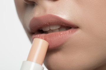 Naklejka premium Close up of mouth of thoughtful girl is applying hypoallergenic balm for lips. Isolated background. Beauty concept
