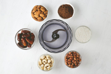 Ingredients for energy bites: nuts, dates, cocoa powder and coconut flakes with food processor on white table. - 196891830