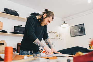 Leather craftsman working making measupenets in patterns at table in workshop studio