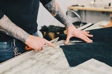 Closeup portrait of unrecognizable leather craftsman working making measupenets in patterns at table in workshop studio