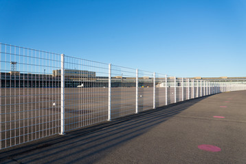 Fototapeta na wymiar BERLIN, GERMANY - DECEMBER 2017 : Iron fence separate park from building of Tempelhofer Feld, former airport, now the airfield and landing field become park, building is museum & events space. 