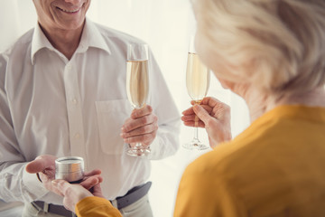 Happy elderly people standing with champagne while celebrating engagement. Male person giving jewelry box to woman