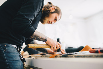Leather craftsman working with leather using hammer. Working process in the leather workshop. Man holding crafting tool and working.