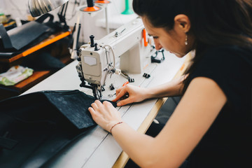 Female artisan threading black leather on sewing machine, close up