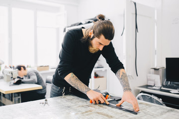 Leather craftsman working making measupenets in patterns at table in workshop studio