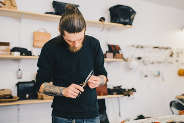 Working process of the leather bag in the leather workshop. Man holding crafting tool and working. Work table background.