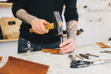 Close up of a leather craftsman working with leather using hammer. Working process in the leather workshop. Man holding crafting tool and working.