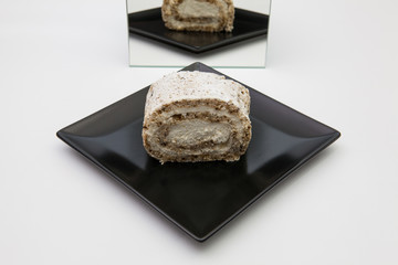 One piece of walnut roll with whipped cream on a black plate.