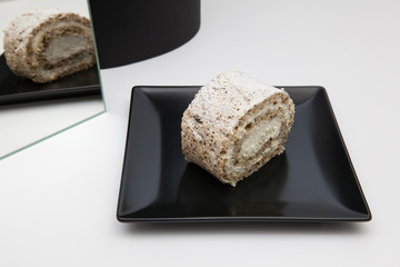 One piece of walnut roll with whipped cream on a black plate.