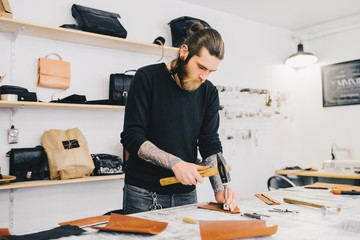 Leather craftsman working with leather using hammer. Working process in the leather workshop. Man...