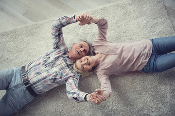 Top view portrait of retired male and female people lying on carpet and holding their hands. They are delighted