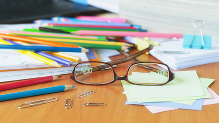 Glasses on the background of colored pencils and paper. The clutter on the desktop. 