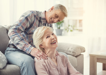 Relaxing procedure. Mature husband massaging wife shoulders at home. They are laughing