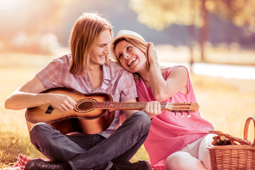 Man playing guitar to his girl on a picnic.