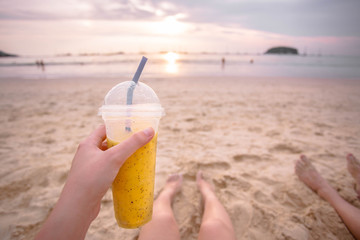 Tropical mango and passion fruit shake in the woman hand on the sunset background on the beach. Thailand, Phuket.