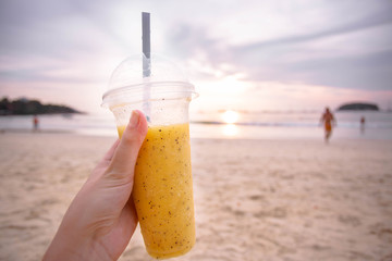 Tropical mango and passion fruit shake in the woman hand on the sunset background on the beach. Thailand, Phuket.