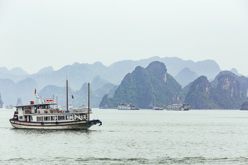 Obraz premium Cruising tourist boat over emerald water with towering limestone islands in the background in summer at Quang Ninh, Vietnam.