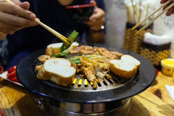 Grilling sliced BBQ pork, vegetables and bread on hot pan by chopstick at the restaurant in Hanoi, Vietnam.