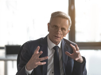 Portrait of concentrated mature male talking story while gesticulating hands in room. Focused...