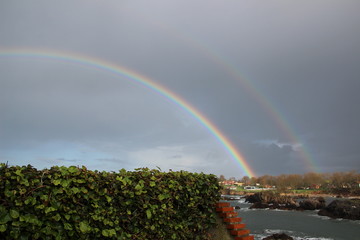 Fototapeta premium wunderschöner Regenbogen über ein paar Häusern und dem Meer an einer kleinen Bucht an der spanischen Atlantikküste