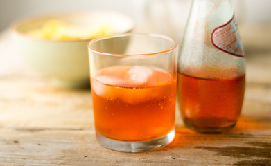 Glass of orange juice / cocktail san pelegrino with ice cubes and a bottle of in the background