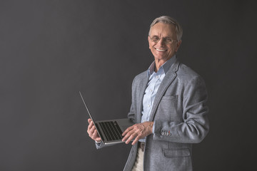 Portrait of outgoing senior male typing in notebook computer while holding it in hand. Technology concept