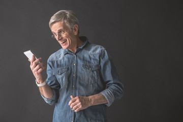Portrait of glad old man typing message in mobile while holding it in hand. Modern appliance concept. Copy space