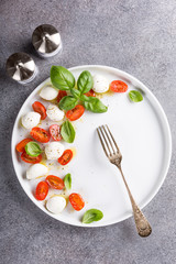 Delicious caprese salad with ripe cherry tomatoes and mini mozzarella cheese balls with fresh basil leaves. Italian healthy food concept with copy space. View from above.