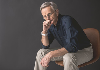Portrait of thoughtful mature male keeping hand near lips while looking at camera. Wistful employer...