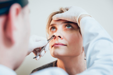 Otolaryngologist examines woman's nose with nasal dilator.