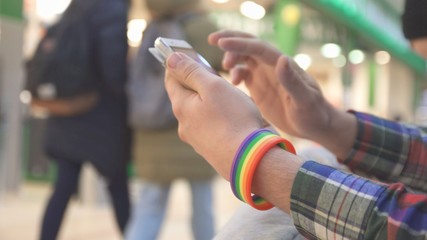 a man with a LGBT symbol wearing a bracelet uses a phone in a shopping center