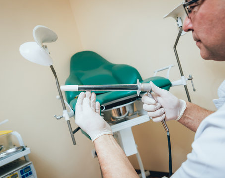 Proctologist holding an anoscope against a proctological chair.