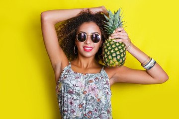 Fashion summer portrait smiling afro american girl in sunglasses and pineapple over yellow background